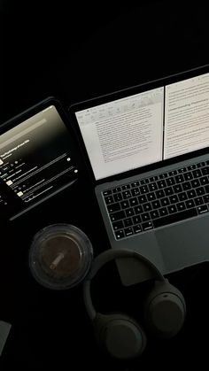 an open laptop computer sitting on top of a desk next to headphones and papers