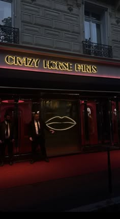 two men in tuxedos are standing outside the entrance to crazy horse paris at night