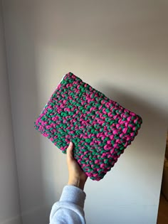 a hand is holding up a pink and green crocheted purse in front of a white wall