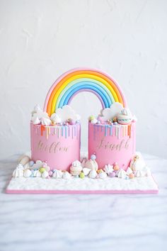 two pink cakes with rainbows and marshmallows on the bottom one has a rainbow cake topper