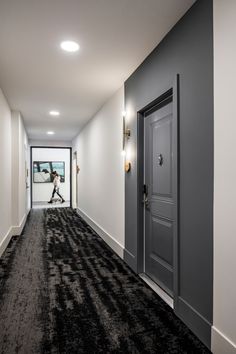 a person walking down an empty hallway with black carpet and white walls, while the door is open