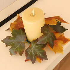 a lit candle surrounded by autumn leaves on a white countertop in front of a window