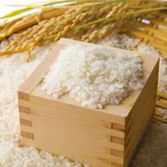 white rice in a wooden box next to stalks of wheat