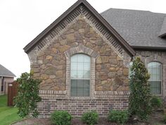 a brick house with two windows and green bushes