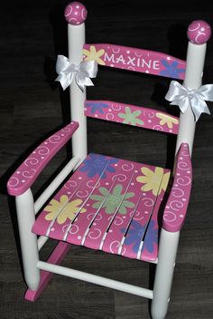 a pink and white wooden rocking chair with flowers on the seat, decorated with bows