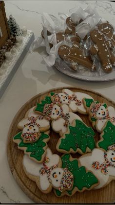 several decorated cookies on a wooden platter next to a plate with christmas trees and snowmen