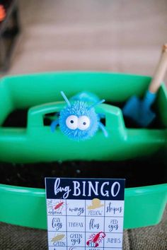 a blue toy bug sitting on top of a green container filled with dirt next to a sign