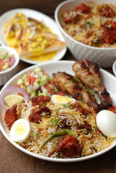 several plates of food including rice, meat and an egg on a wooden table top