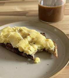 there is a piece of bread with cheese on it next to a cup of coffee