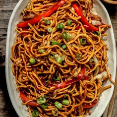 a plate full of noodles with peppers and green onions on the side next to a fork