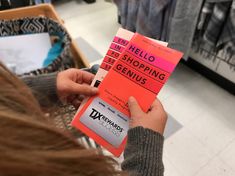 a person holding up a pink and orange sign in a store with other items on the shelves