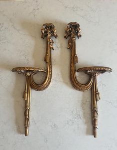 two antique brass sconces with flowers on the handles, mounted against a white marble wall