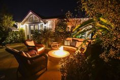 an outdoor fire pit in the middle of a yard with chairs around it at night