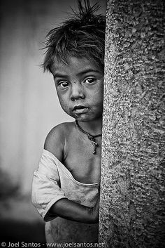 black and white photograph of a young boy peeking out from behind a tree