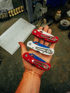 three different types of scissors held in someone's hand with tools on the table behind them