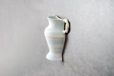 a small white vase on the wall with a hook in it's middle,