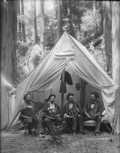 an old black and white photo of men sitting in front of a tent