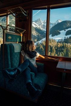 a woman is sitting on a train looking out the window at mountains and snow capped peaks