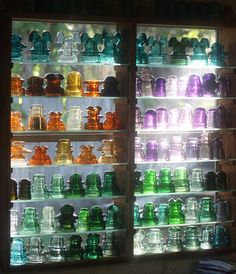 many different colored glass vases on display in a store window with light coming through them