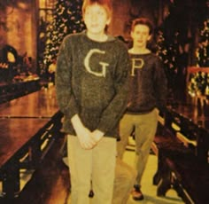 two young men standing next to each other in front of a christmas tree with lights