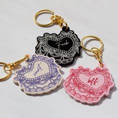 three keychains with different designs on them, one has a heart and the other has a monogram