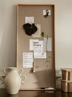 a white vase sitting on top of a table next to a cork board with papers