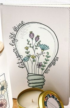 a card with a light bulb and flowers in it next to a small candle on a table