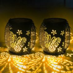 two lit candles sitting on top of a table next to each other with butterflies on them