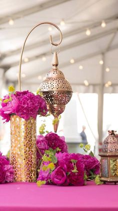 pink flowers and gold vases on a table with arabic writing in the middleground