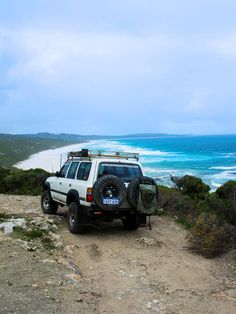 a white truck parked on top of a dirt road next to the ocean and beach