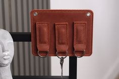 three hooks are attached to the back of a brown leather case on a mannequin's head