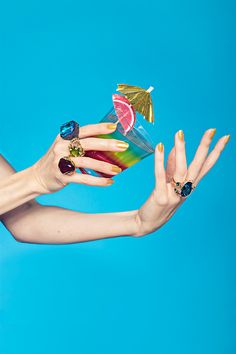 a woman's hand holding a cocktail glass with fruit on it and two rings