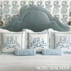 a bed with blue and white pillows on top of it next to a wallpapered headboard