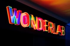 the word wonderland is lit up in bright neon letters on a black wall with colorful lights behind it