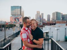 two men hugging each other on a balcony in front of a cityscape with tall buildings