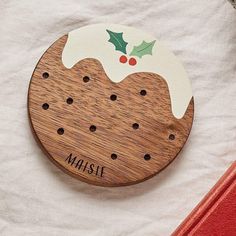 a wooden christmas ornament with holly and mist on it's top, sitting on a white sheet