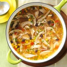 a bowl of soup with chicken, corn and broth on a table next to a spoon