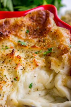 a red dish filled with mashed potatoes covered in parmesan cheese and herbs