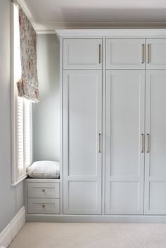 an empty room with white cabinets and drawers in the corner, along with a window seat