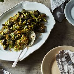 a white plate topped with broccoli on top of a table next to plates