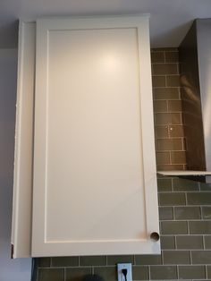 a white cabinet in a kitchen with green tiles on the wall behind it and a light above