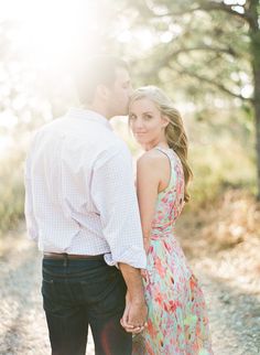 a man and woman standing next to each other on a dirt road in front of trees