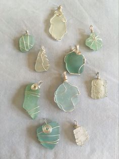 seven different sea glass pendants sitting on a white cloth covered table with silver wire