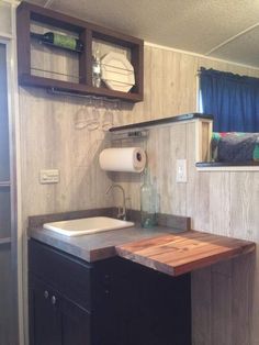 a kitchen area with sink, counter and shelf above it in a trailer or home