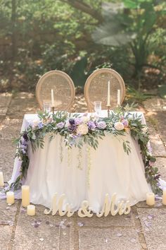 a table with flowers and candles on it that says mr & mrs surrounded by greenery