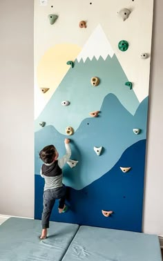 a young boy climbing up the side of a wall with rocks on it and mountains in the background