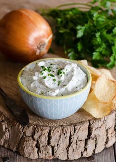 a bowl of dip next to chips and an onion on a wooden board with parsley