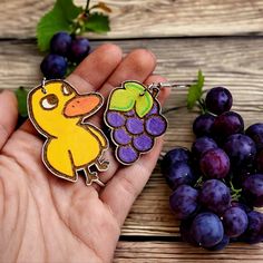 a hand holding a yellow duck next to some purple grapes on a wooden table with green leaves