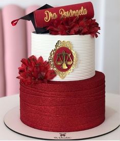 a red and white tiered cake with flowers on top, topped with a judge's gaven