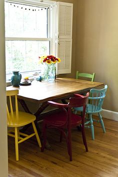 a dining room table with four chairs and a vase filled with flowers on the window sill